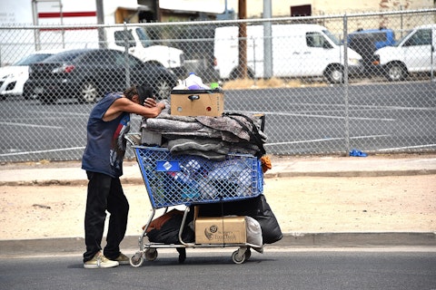 homeless man leaning on shopping cart full of items