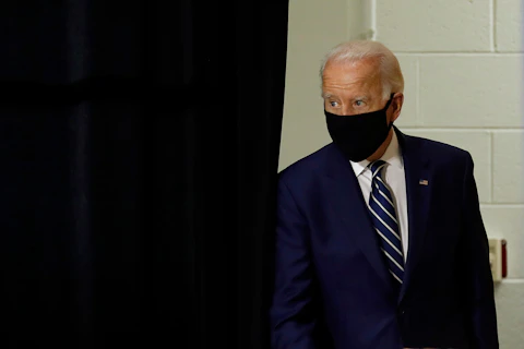 Joe Biden walking out from a stage curtain wearing a face mask