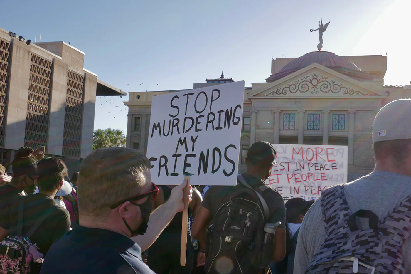 man holding sign at Phoenix protest that says "stop murdering my friends"
