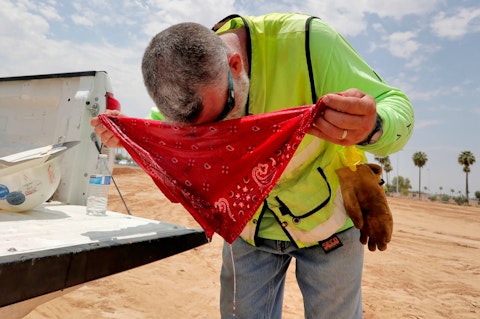 man wearing construction vest wrapping a bandana dripping with water around his forehead