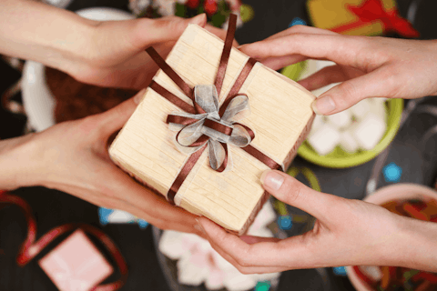 a pair of hands handing a present with a bow to another pair of hands