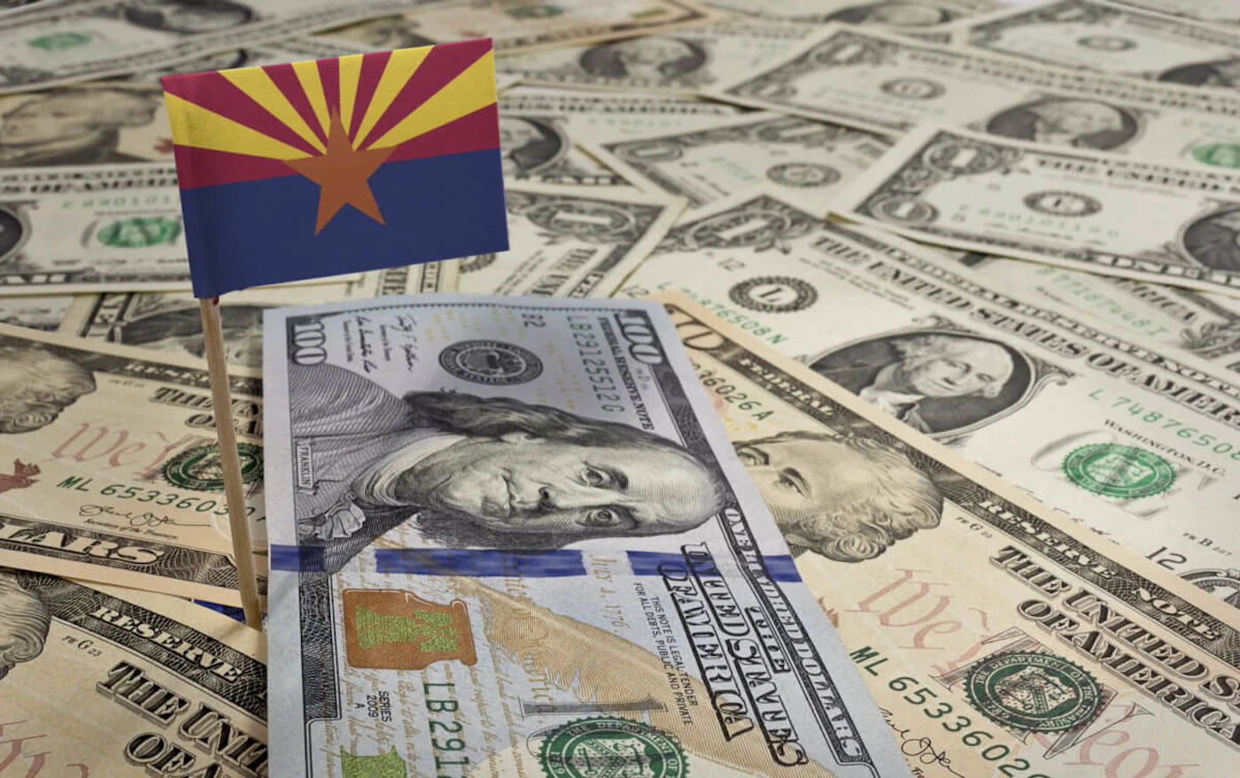 100 dollar bill on top of fanned out one dollar bills with an AZ state flag on top