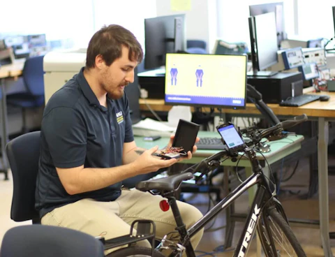 young man sits in front of a computer and a bike
