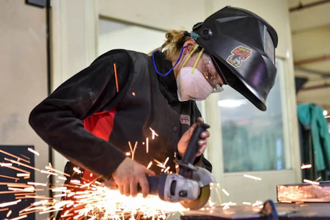 woman in safety gear cutting a material with sparks flying