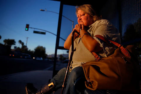 OCTOBER 27, 2014. TUCSON, AZ.  Karen Slone (cq), age 53, waits on a Tucson bus bench near her apartment.  A special boot protects her foot after radical surgery at Tucson Medical Center.   Slone lost part of the foot to a diabetic induced infection.  Periodic doctor checkups that might have caught the infection had lapsed after she lost her health insurance and couldn't qualify for Arizona Medicaid.  (Photo by Don Bartletti/Los Angeles Times via Getty Images)