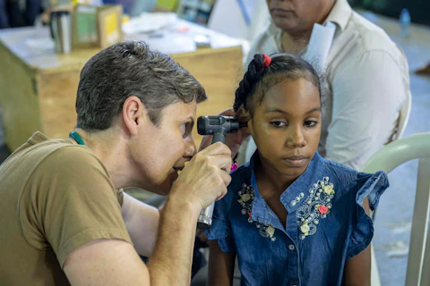 Navy Capt. Jill Emerick, a doctor with the hospital ship USNS Comfort, gives a girl a checkup in this 2019 photo from Santo Domingo, Dominican Republic, part of the ship's mission of providing care to help allies' national medical systems. (Photo by Petty Officer 2nd Class Bobby J. Siens/US Navy Southern Command) 
