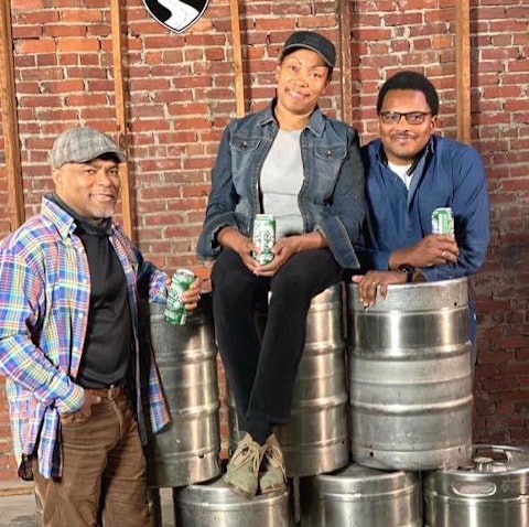 Carl (left) and Pernell Beatty (right) flank their sister Celeste, the owner of Harlem Brew South, in her taproom. The warehouse is the site of Operation Dixie, a historical and successful labor campaign in 1946. More than 10,000 tobacco workers, mostly women, gathered from around the state and voted to unionize for better working conditions. Harlem Brew's lager is named '1946' in tribute.