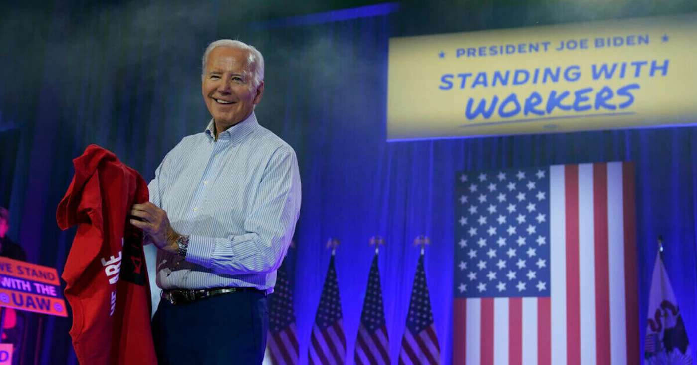 President Joe Biden puts on a UAW Local 1268 shirt before speaking to United Auto Workers on Thursday in Belvidere, Ill. (AP Photo/Evan Vucci)