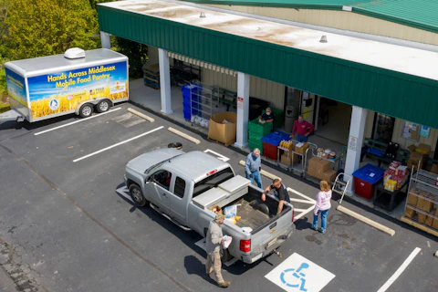 This aerial view shows Hands Across Middlesex Food Pantry volunteers load packed bags of food into vehicles at their drive up food pantry distribution center Tuesday April 28, 2020, in Locust Hill, Va. AP Photo/Steve Helber)