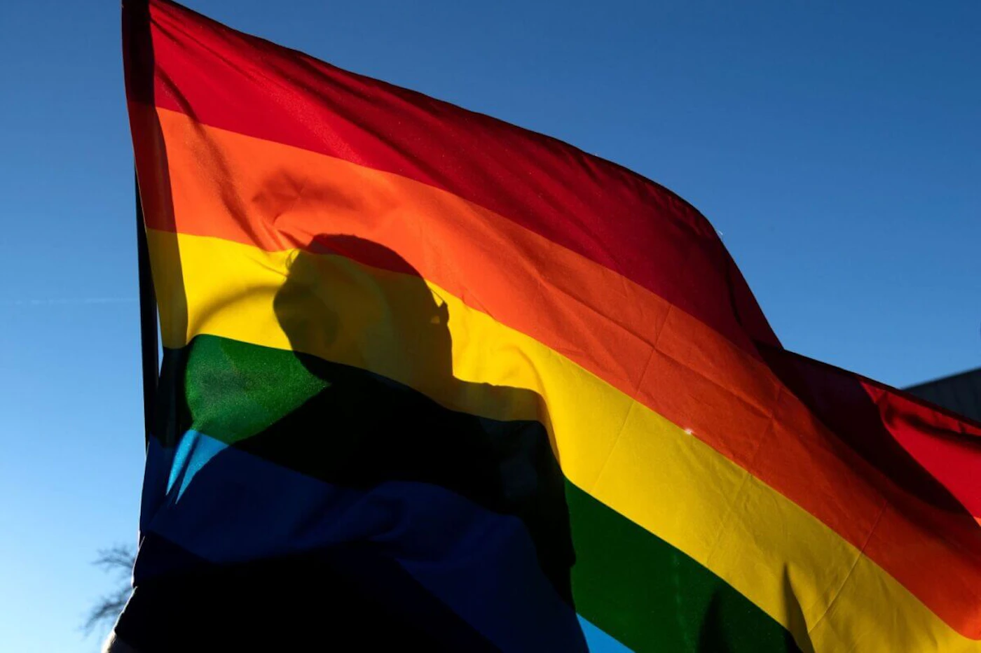 TOPSHOT - A commuity members silhouette is seen through a Pride flag while paying their respects to the victims of the mass shooting at Club Q, an LGBTQ nightclub, in Colorado Springs, Colorado, on November 20, 2022. - At least five people were killed and 18 wounded in a mass shooting at an LGBTQ nightclub in the US city of Colorado Springs, police said on November 20, 2022. (Photo by Jason Connolly / AFP) (Photo by JASON CONNOLLY/AFP via Getty Images)