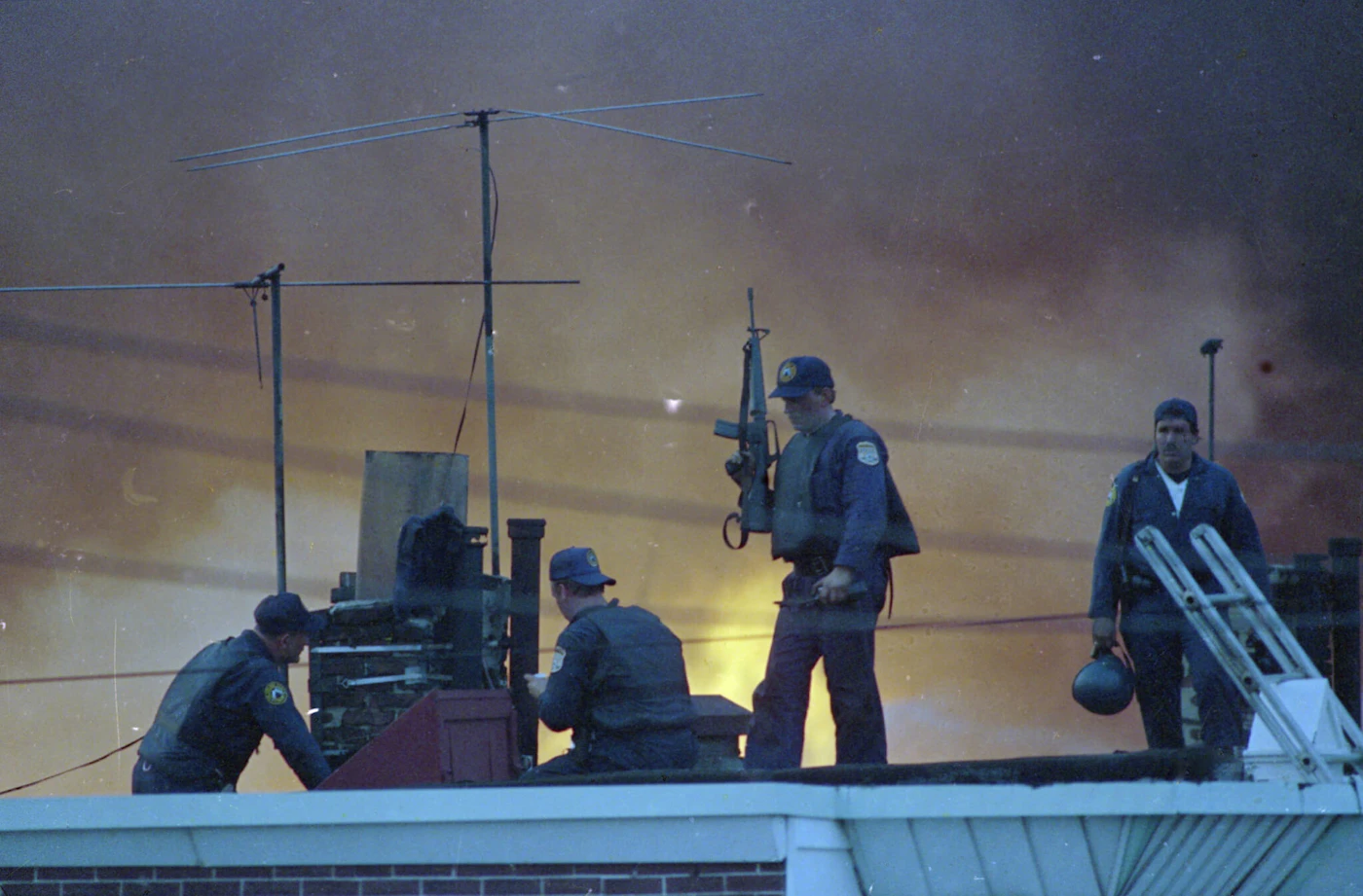 Armed Philadelphia police officers man a rooftop as the sky is illuminated by the flames from a neighborhood in West Philadelphia, Pa., that burned after police dropped a bomb on a building occupied by members of anarchist group MOVE, May 13, 1985.  (AP Photo/George Widman)
