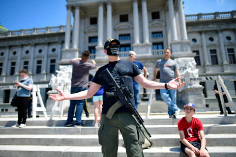 HARRISBURG, PA - MAY 15: A man with an assault rifle reacts while joining demonstrators outside the Pennsylvania Capitol Building to protest the continued closure of businesses due to the coronavirus pandemic on May 15, 2020 in Harrisburg, Pennsylvania. (Photo by Mark Makela/Getty Images)