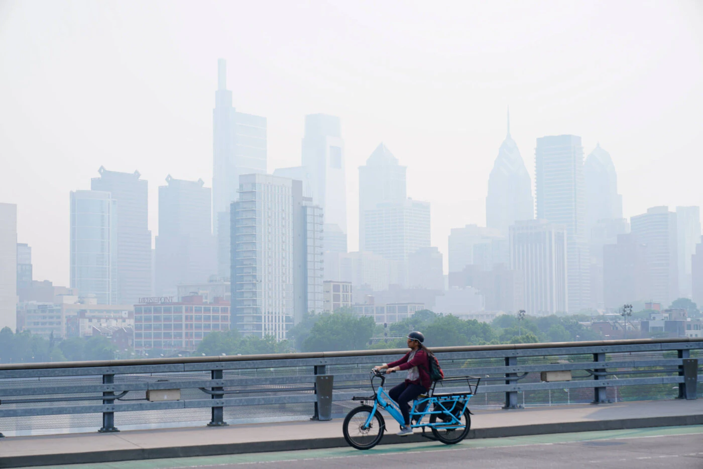 A person cycles past the skyline in Philadelphia shrouded in haze, Thursday, June 8, 2023. Intense Canadian wildfires are blanketing the northeastern U.S. in a dystopian haze, turning the air acrid, the sky yellowish gray and prompting warnings for vulnerable populations to stay inside. (AP Photo/Matt Rourke)