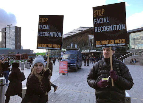 In this Feb. 11, 2020, file photo, Silkie Carlo, left, demonstrates in front of a mobile police facial recognition facility outside a shopping centre in London. A Black man who says he was unjustly arrested because facial recognition technology mistakenly identified him as a suspected shoplifter is calling for a public apology from Detroit police. And for the department to abandon its use of the controversial technology. (AP Photo/Kelvin Chan, File)