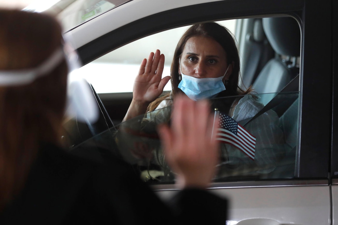 In this Friday, June 26, 2020 photo, U.S. District Judge Laurie Michelson, left, administers the Oath of Citizenship to Hala Baqtar during a drive-thru naturalization service in a parking structure at the U.S. Citizenship and Immigration Services headquarters on Detroit's east side. The ceremony is a way to continue working as the federal courthouse is shut down due to Coronavirus. The U.S. has resumed swearing in new citizens but the oath ceremonies aren't the same because of COVID-19 and a budget crisis at the citizenship agency threatens to stall them again.  (AP Photo/Carlos Osorio)